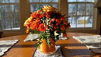 Beautiful, shiny, orange pot with colorful flowers in light, on the table near the windows