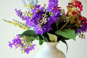 Bouquet of the beautiful and colorful flowers with green leaves, in the vase, at white background