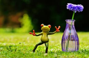 funny figurine of a frog near a vase with a flower
