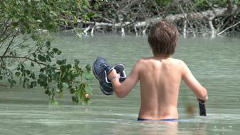 child carries shoes in the river