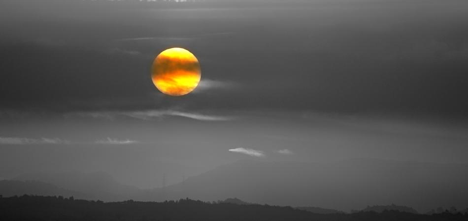 yellow Sun in grey sky over rural landscape