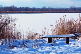 snow on a bench against the background of a frozen lake