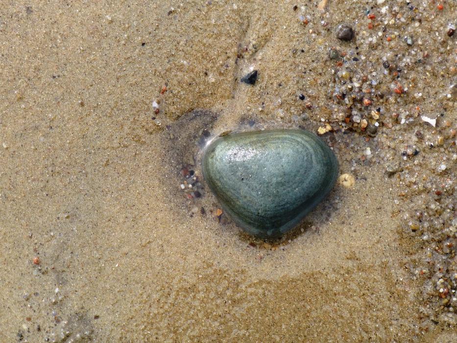 green stone in sand with water