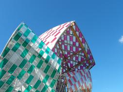 Green, purple and silver Vuitton Foundation building, at blue sky with white clouds on background, in Paris, France