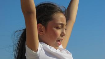 photo of a girl with hands up against a blue sky