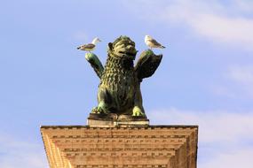 Beautiful monument of a creature, with the birds, at blue sky with white clouds on background