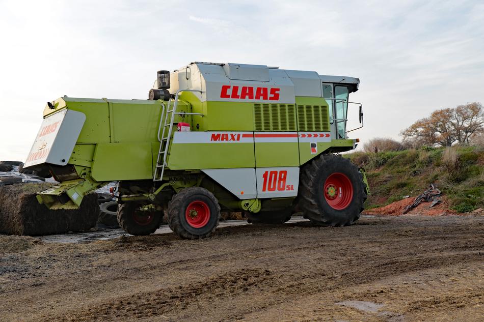 Colorful combine machine on the field near the plants, under the blue sky with clouds