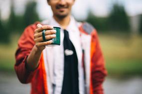 Smiling man, with the green cup in the hand, at blurred background