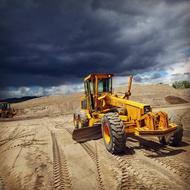 Yellow scraper machine, on the sand landscape, under the clouds