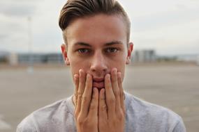 young man holds his face with his hands