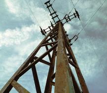 Low angle shot of the rusty electricity power line, with the wires, under the sky with clouds