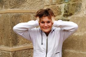 Portrait of the smiling girl in white sweatshirt, near the stone wall