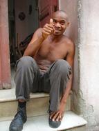 Smiling man, sitting on the stairs of the house in Cuba