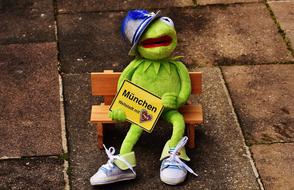 green Kermit sits on a bench holding a sign