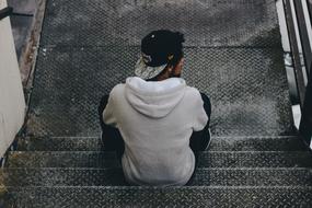 young man in Cap sits on metal stairs