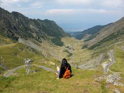 young Girl with backpack sits on Mountain side at scenic landscape