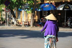 asian woman in traditional Conical hat riding bicycle in city, Vietnam, Há»i An