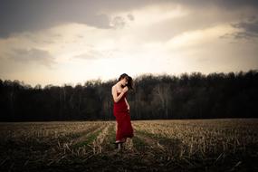 girl in a red dress on arable field in the evening