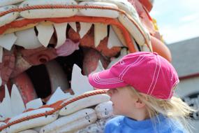 child Girl in pink cap looking at monster Fish playground at sea