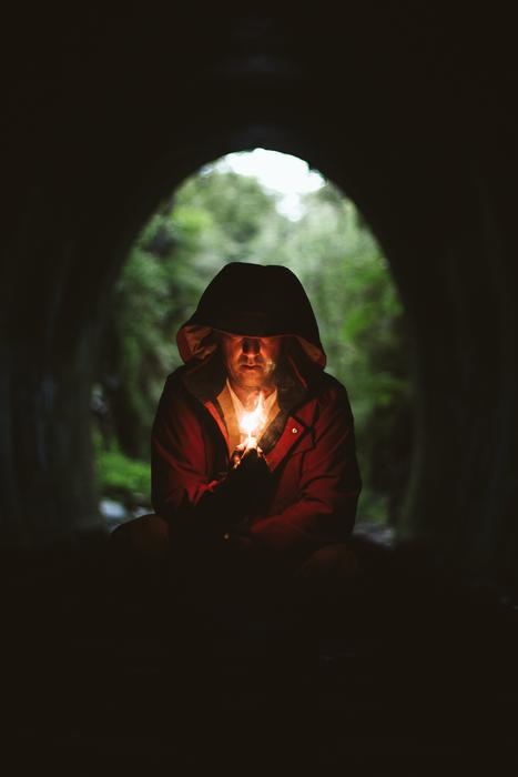 Man in hood, with the flame, in the building, at background with the green trees
