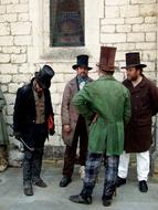four men in victorian clothing at old brick wall