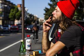 young man in red hat smoking at table on street, usa, california, San Francisco