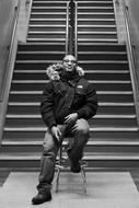 young african man in winter clothing sits on chair in front of stairway, Monochrome