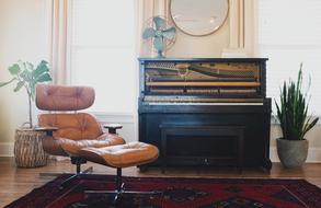 Colorful interior of the apartment, with the brown chair, piano with the fan, among the green plants