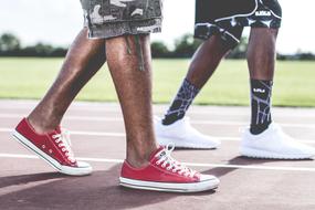 two pair of male legs in sneakers walking on stadium