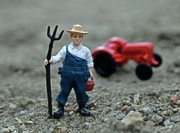 Figure of the farmer in hat, with the pitchfork, near the red tractor, among the colorful rocks