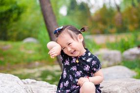 happy asian baby girl sits on stone in park