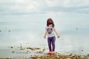 child Girl stands on beach back to Water