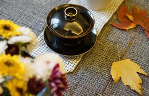 Tea Cup with cover, autumn flowers and leaves on table at Home