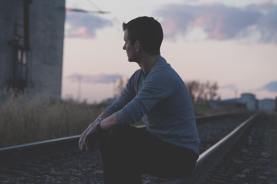 young man sits on railroad tracks