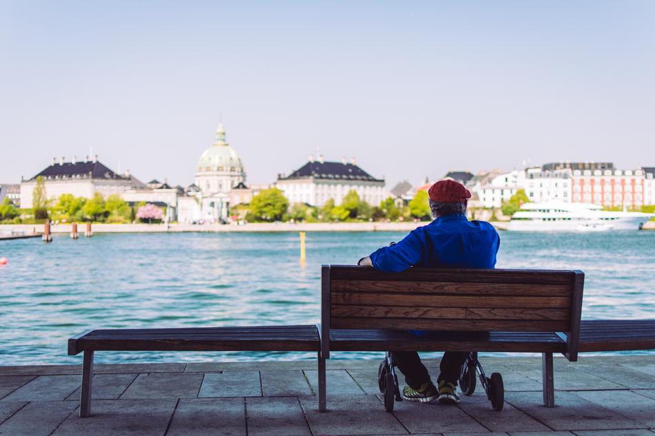 man sits on Bench on waterfront in view of old city