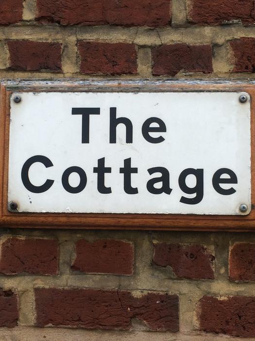 White and black 'The Cottage' sign on the brick wall in England