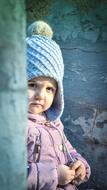 girl in autumn hat peeks around the corner