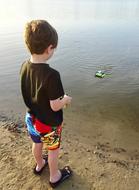 toddler boy plays with toy boat at water