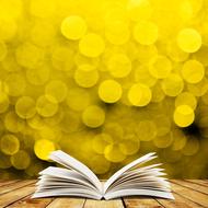 Open book on the wooden surface at yellow background with bokeh lights