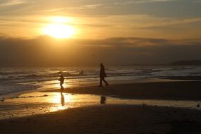 woman and child walking on beach to water at sunset