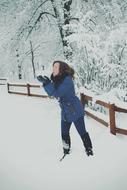 Girl playing with the beautiful snow, on the path, among the fence and trees, in the winter