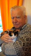 old man holds tricolor cat at breast