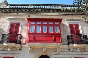 Beautiful house with red balcony and shutters on the facade, in Malta