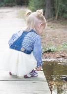 little girl with ponytails crouched on the shore of the pond