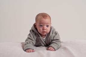 Baby boy in grey clothing on white blanket