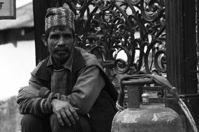 Poor adult dark skin Man sits at wrought iron fence