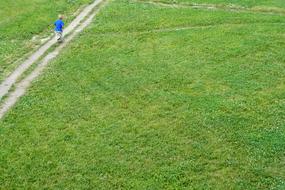 a child walks along a road along a green field