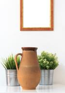clay jug in front of plants in buckets at white wall