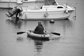 Man in Rowing boat on water near motor boat, Black And white