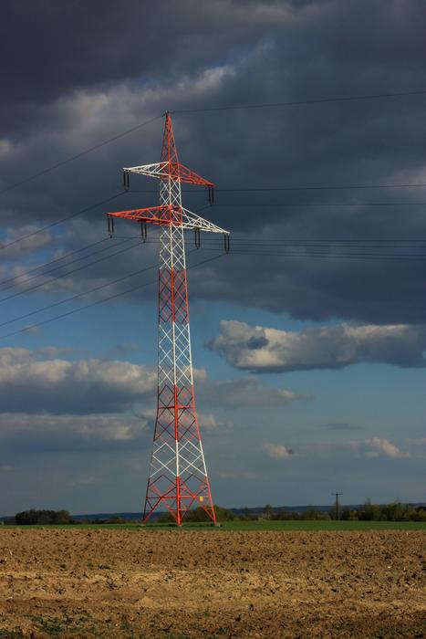 Red and white current tower, on the beautiful and colorful field, under the clouds